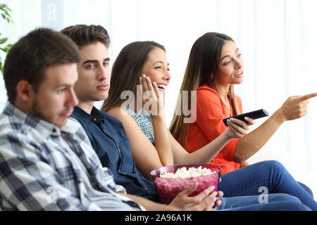 Girls watching romantic movie with their bored boyfriends sitting on a couch in the living room at home Stock Photo