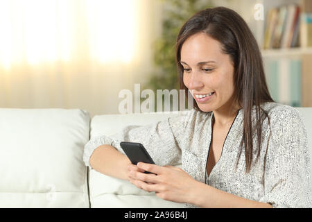 Happy woman uses smart phone sitting on a couch in the living room at home Stock Photo