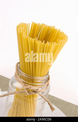 Dried linguini pasta in a transparent glass jar that has a twine ribbon tied around it. Stock Photo