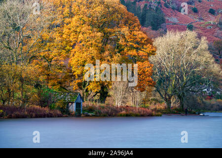 Old boathouse on Grasmere Lake surrounded by autumn colour in the Lake District National Park. Long exposure with smooth water Stock Photo