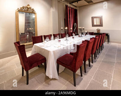 Long formal dining table in an elegant restaurant set with a white cloth, cutlery and glassware with burning candles in candelabra Stock Photo