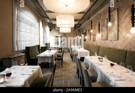 Receding view of rows of empty restaurant tables set with glassware and silverware in an upmarket elegant restaurant illuminated by lamps Stock Photo