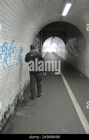 Unidentifiable man using mobile phone whilst walking along underneath the railway bridge in Leeman Road, York, North Yorkshire, England, UK. Stock Photo