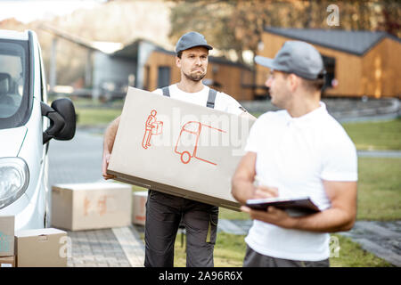 Two male couriers delivering goods by cargo van vehicle, unloading cardboard parcels from a car outdoors Stock Photo
