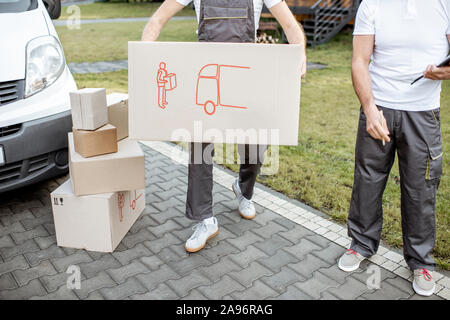 Delivery men moving cardboard boxes outdoors, delivering goods with cargo vehicle, close-up on boxes with no face Stock Photo