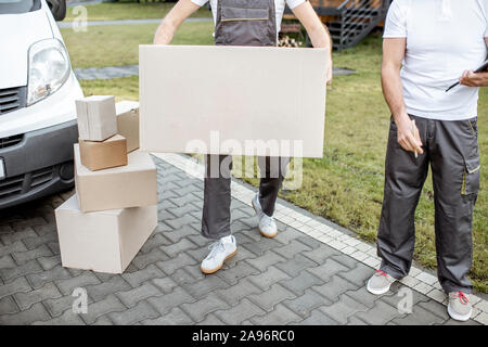 Delivery men moving cardboard boxes outdoors, delivering goods with cargo vehicle, close-up on boxes with blank space Stock Photo