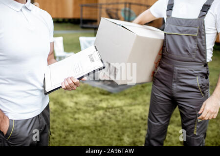 Delivery men with checklist and cardboard boxes outdoors, close-up view with no face Stock Photo