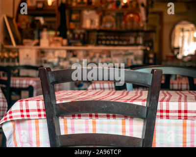 A chair near a free table in a restaurant or cafe. Red checkered textile tablecloth. Classic wooden chair back in brown color. Blurry showcase and bar Stock Photo