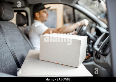 Delivery man driving cargo vehicle with parcels on the passenger seat, image focused on the cardboard boxes with blank space Stock Photo