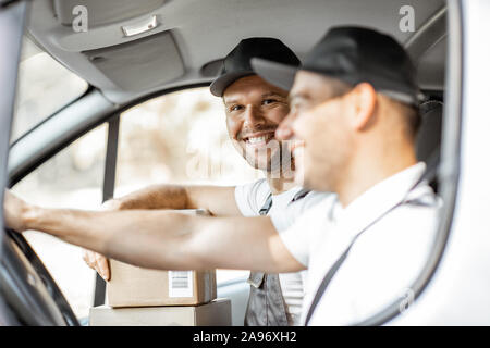 Two cheerful delivery company employees in uniform having fun while driving a cargo vehicle, delivering goods to the customers Stock Photo