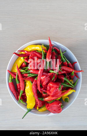 Bowl of fresh mixed chili peppers, red, orange and yellow hot peppers on a wooden table viewed from above, habanero, lemon drop, thai peppers Stock Photo
