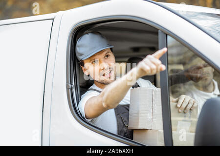 Delivery company employees driving cargo vehicle, delivering goods to the customers, handsome courier pointing on the way forward Stock Photo