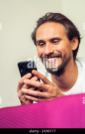 Photo of a handsome young man that is smiling while holding his mobile phone. Stock Photo
