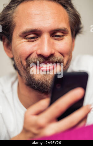 Photo of a handsome young man that is smiling while holding his mobile phone. Stock Photo