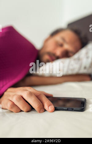 Sleeping young handsome man while holding his mobile phone. Screen on the phone is turned off Stock Photo