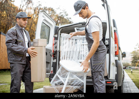 Delivery company employees unloading cargo van vehicle, delivering some goods and furniture to a clients home. Relocation and professional delivery concept Stock Photo