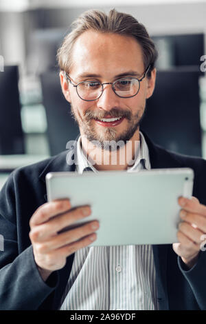 Young handsome man in glasses reading a tablet at work. Stock Photo