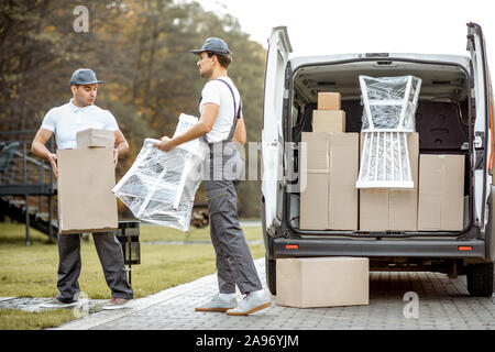 Delivery company employees unloading cargo van vehicle, delivering some goods and furniture to a clients home. Relocation and professional delivery concept Stock Photo