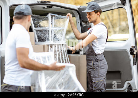 Delivery company employees unloading cargo van vehicle, delivering some goods and furniture to a clients home. Relocation and professional delivery concept Stock Photo