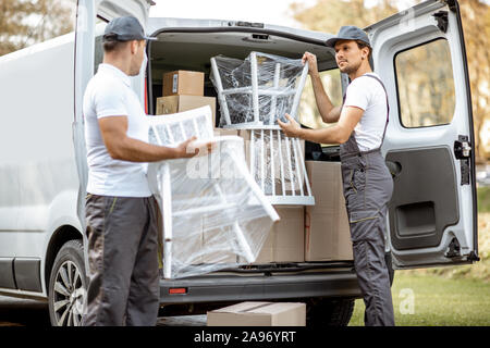 Delivery company employees unloading cargo van vehicle, delivering some goods and furniture to a clients home. Relocation and professional delivery concept Stock Photo