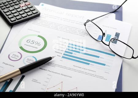 Mockup financial charts report sheet with visible pen, calculator and eyeglasses on white desk. Accounting, business, finance, tax and office concepts Stock Photo