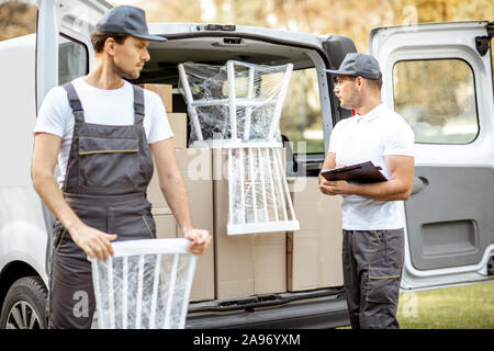 Delivery company employees unloading cargo van vehicle, delivering some goods and furniture to a clients home. Relocation and professional delivery concept Stock Photo
