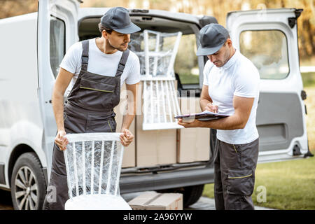 Delivery company employees unloading cargo van vehicle, delivering some goods and furniture to a clients home. Relocation and professional delivery concept Stock Photo