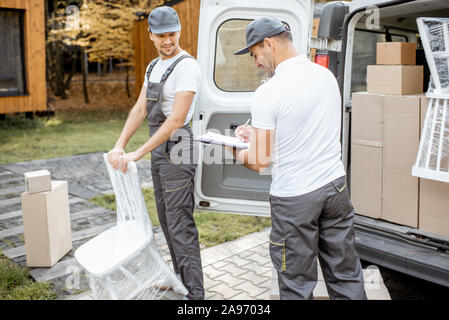 Delivery company employees unloading cargo van vehicle, delivering some goods and furniture to a clients home. Relocation and professional delivery concept Stock Photo