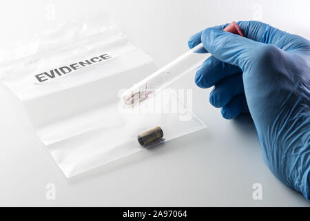 Closeup of forensic scientist's hand in blue rubber glove holding glass tube over evidence bag with 9 mm bullet case. Crime, forensic science Stock Photo