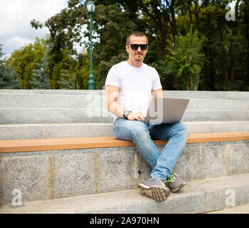 Man with laptop sitting on bench in modern urban park Stock Photo