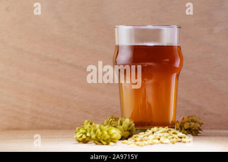 Beer in a glass with barley and hops on wooden background. Craft beer, brewery and alcohol beverage concepts. Stock Photo