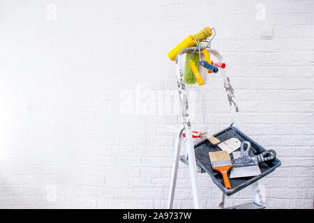 Painted stepladder with black tray, paint bucket, set of brushes and multi-colored spatulas for repair in the form of an abstract art easel shape. The Stock Photo