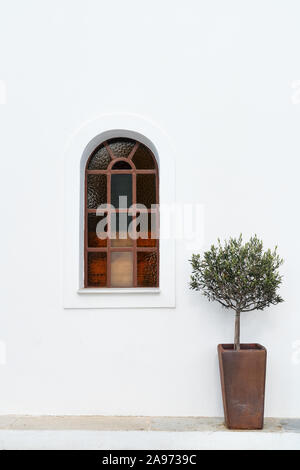 Arched top plain stained glass window on a whitewashed building. Stock Photo