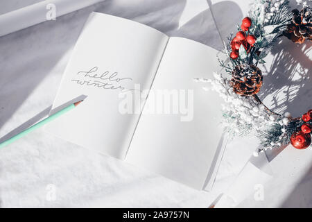 Hello winter concept. The inscription in a white notebook on a white background. Decor from Christmas decorations. Lettering Seasons Minimalism. Stock Photo