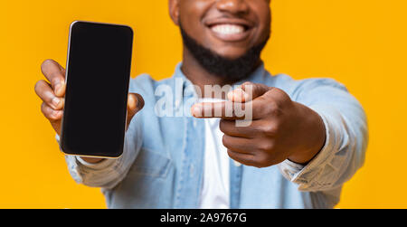 Unrecognizable afro guy holding smartphone with black screen and pointing on it, selective focus on hands with phone, panorama Stock Photo