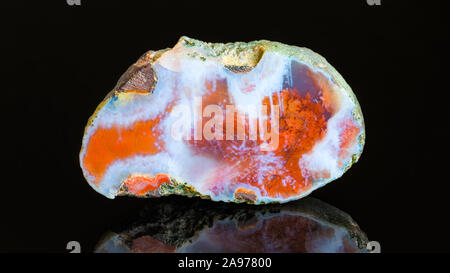 Polished agate precious stone cross section and reflection on black background. White blue gemstone detail, rust brown fibrous spots on smooth surface.