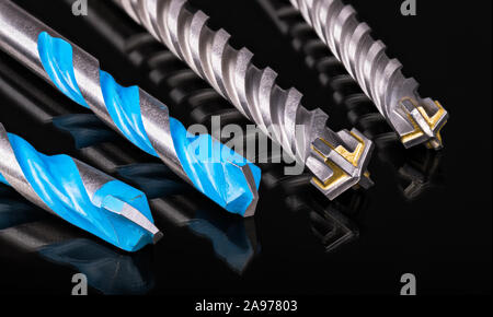 Drill bits cutting edges. Artistic detail of hard spiral fluted tools for drilling of concrete masonry or stone. Reflection on shiny black background. Stock Photo