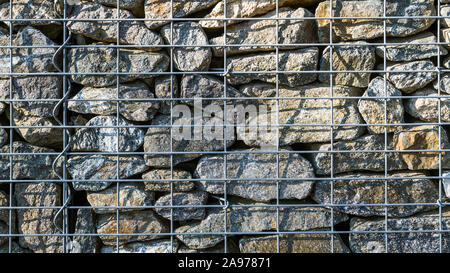 Gabion retaining wall texture. Closeup of stacked stones in wire mesh cage. Background of protective fence detail made from sunlit gray pieces of rock. Stock Photo