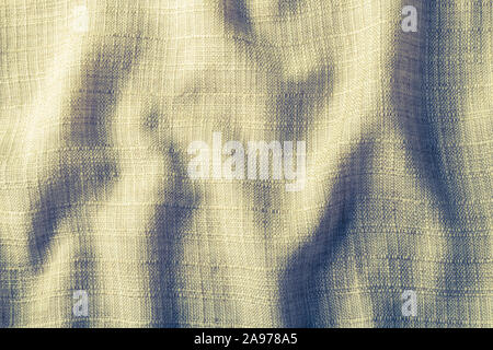 Dynamic wavy abstract textile background. Woven cloth with light and shadows in folds. Creased yellowish fabric closeup. Grid pattern on rough texture. Stock Photo