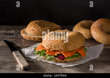 Bagel sandwich with cream cheese, smoked salmon and vegetables on wooden table Stock Photo