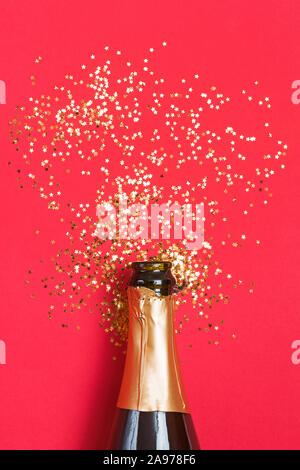 Champagne bottle with golden star shaped confetti on red background. Stock Photo