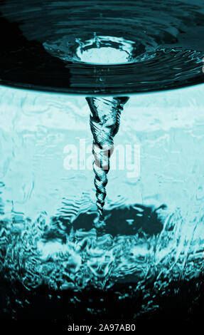 Vortex of overflowing water in rotating glass tube, water glass with rotating column of air, water tube with blue vortex storm of air, decorative kine Stock Photo