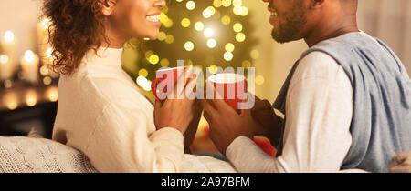 Couple enjoying hot coffee on Christmas eve, talking to each other against xmas tree Stock Photo