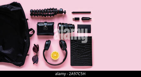 Modern black accessories, gadgets and lemon slice on pink background, top view. Flat lay composition with citrus fruit, headphones, notebook, flash dr Stock Photo