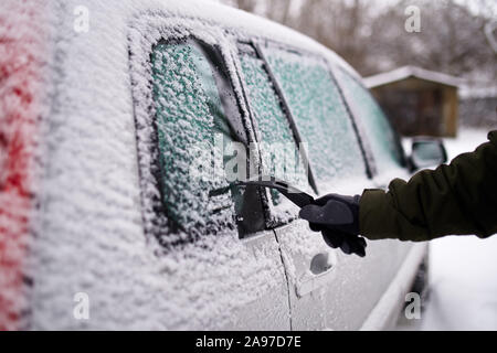 Cleaning the side car windows of snow with ice scraper before the trip. Man removes ice from car windows. Male hand cleans car with special tool at Stock Photo