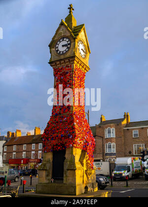 The town clock in the Market Place in Thirsk North Yorkshire UK decorated with knitted poppies for Remembrance day for war dead Stock Photo