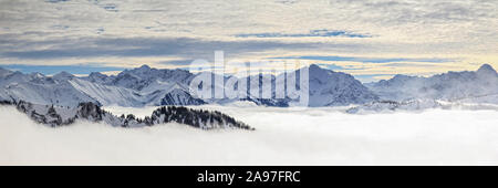 Steep mountain slopes and mountain ranges in low lying valley fog and trees shrouded in mist. Scenic snowy winter landscape in Alps, Allgau, Bavaria, Stock Photo