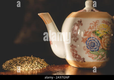 Natural thyme leaves, a white teapot and a white cup on a brown wooden table. Black background Stock Photo