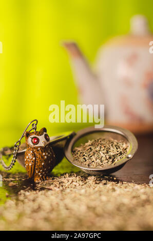 Tea infuser / filter with natural thyme leaves and a white teapot behind. Preparation of natural and healthy thyme tea on a brown wooden table. Green Stock Photo