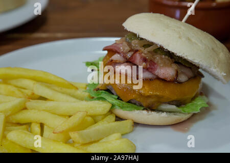 Isolated image of veal burger with french fries served on white plate on wooden background Stock Photo